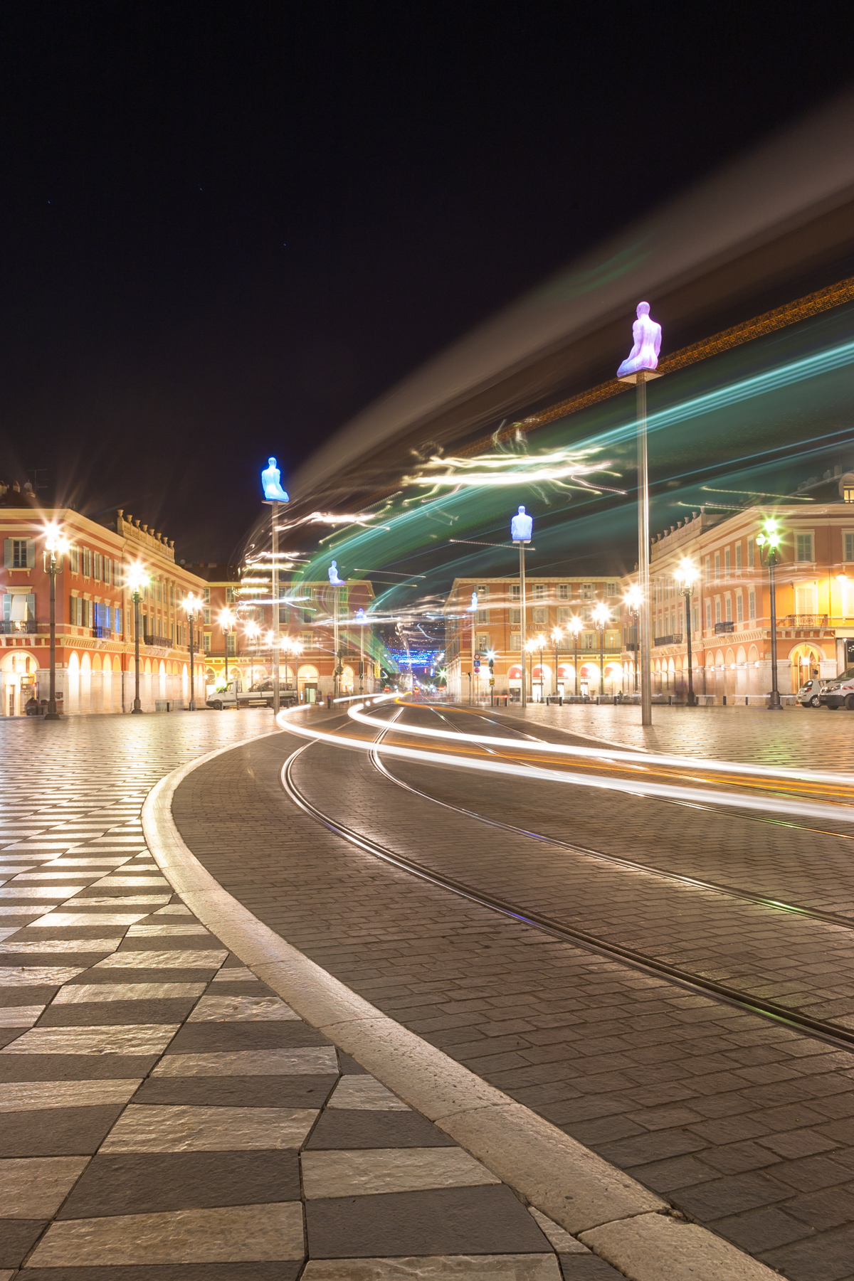 Place Masséna showing art installation of giant glowing buddhas on plinths by Jaume Plensa and long exposure of tram lights