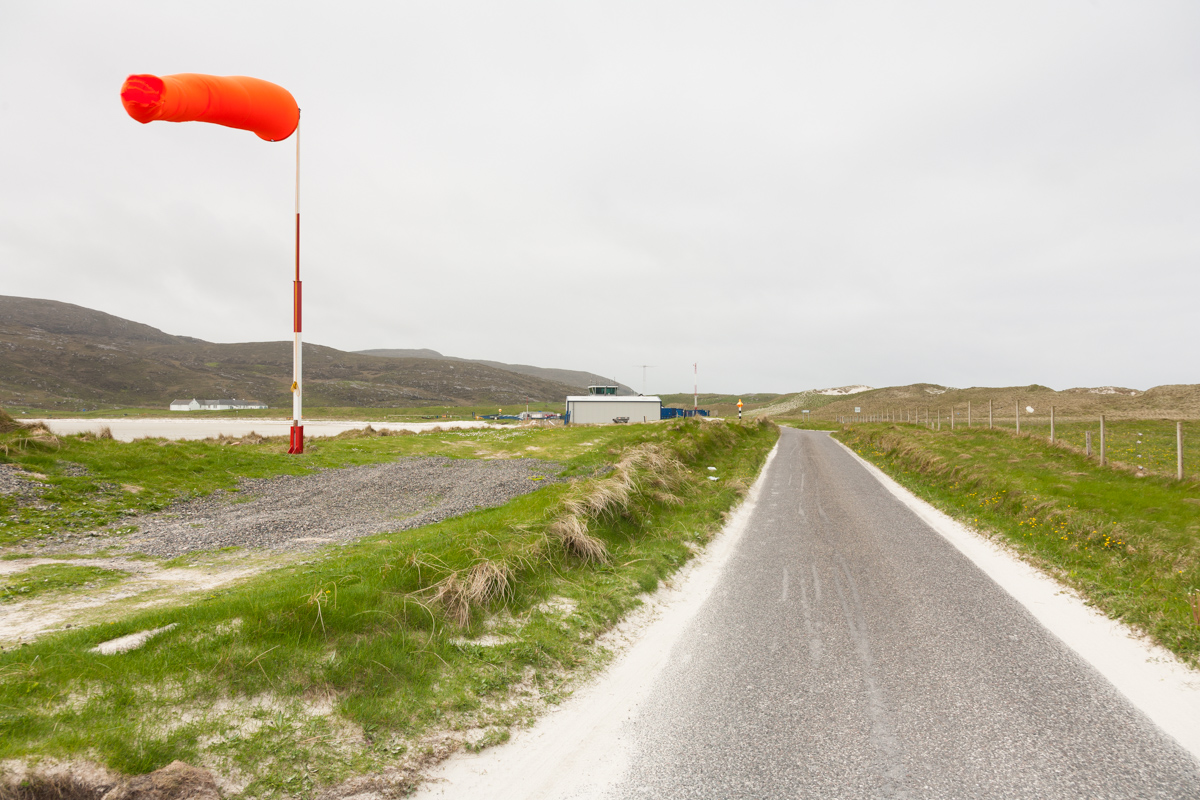 The Barra airport windsock in strong winds and the road leading up to the airport. The landing strip on the beach is just visible on the left.