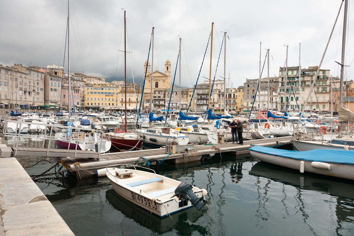 Photo taken in Bastia Corsica down by the harbour showing a profusion of boats and with many buildings in the backdrop.
