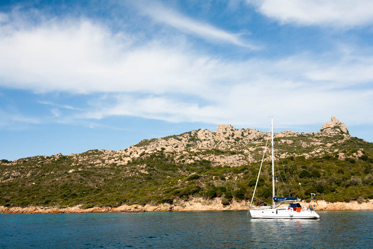 Yacht in harbour near Bonifacio in Corsica, visible in background is rocky coastline and blue sky.