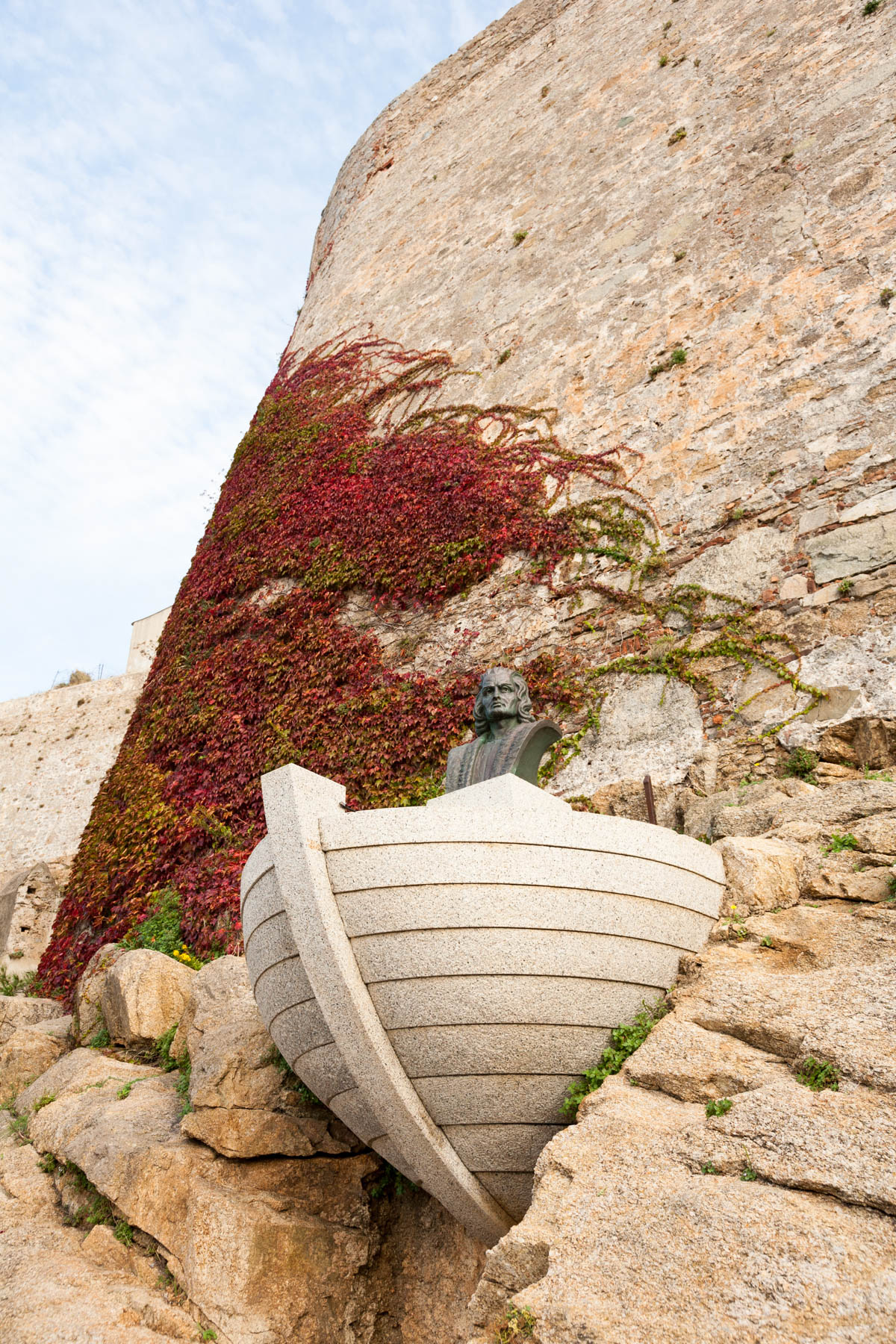 Sculpture of Christopher Columbus, in boat, protuding from wall with red ivy climbing behind.