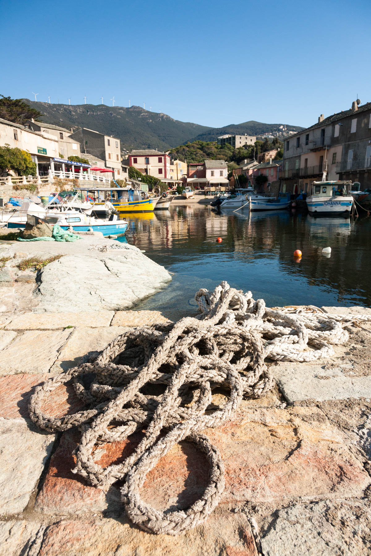 View inland from the Port of Centuri in Corsica, visible are the village, rope in the foreground, fishing vessels and the a wind farm on the hills behind.